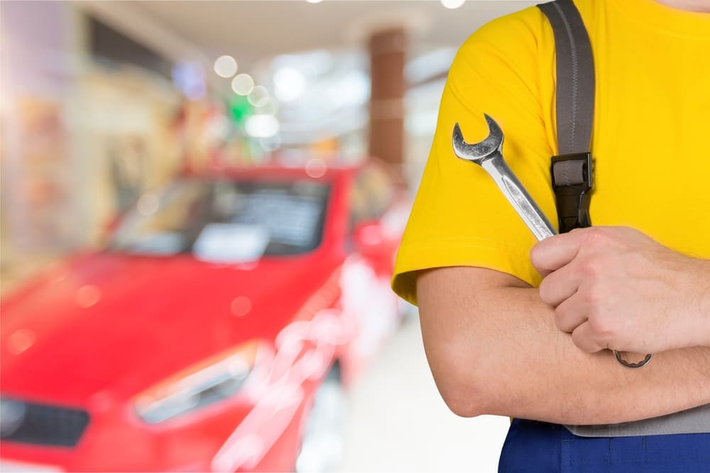 Repair technician holding a wrench with a red sedan in the background.